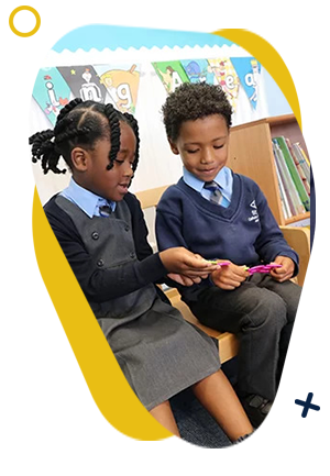 Two young students sat together on a wooden bench, looking at some purple coloured shapes.